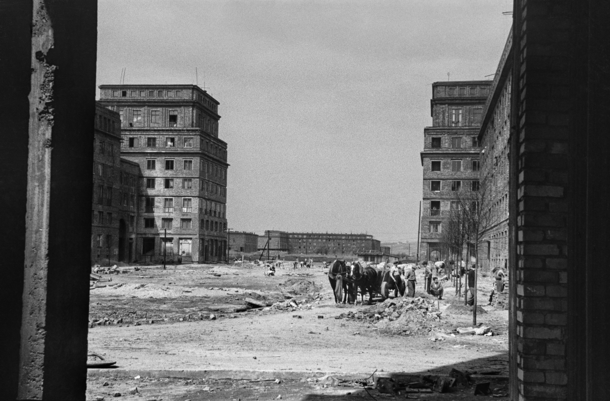 A view of an unfinished, spacious square between monumental residential buildings.