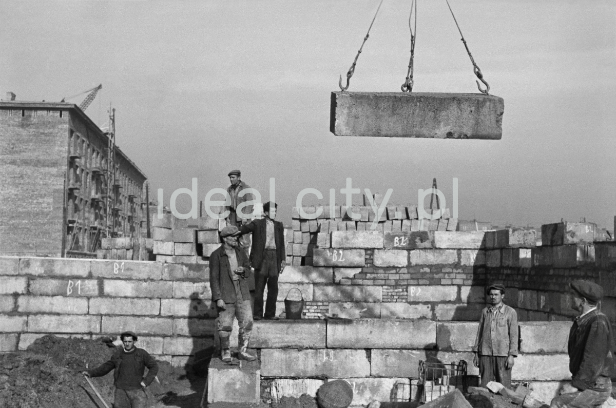 A team of workers is waiting for a prefabricated element fed by a crane.