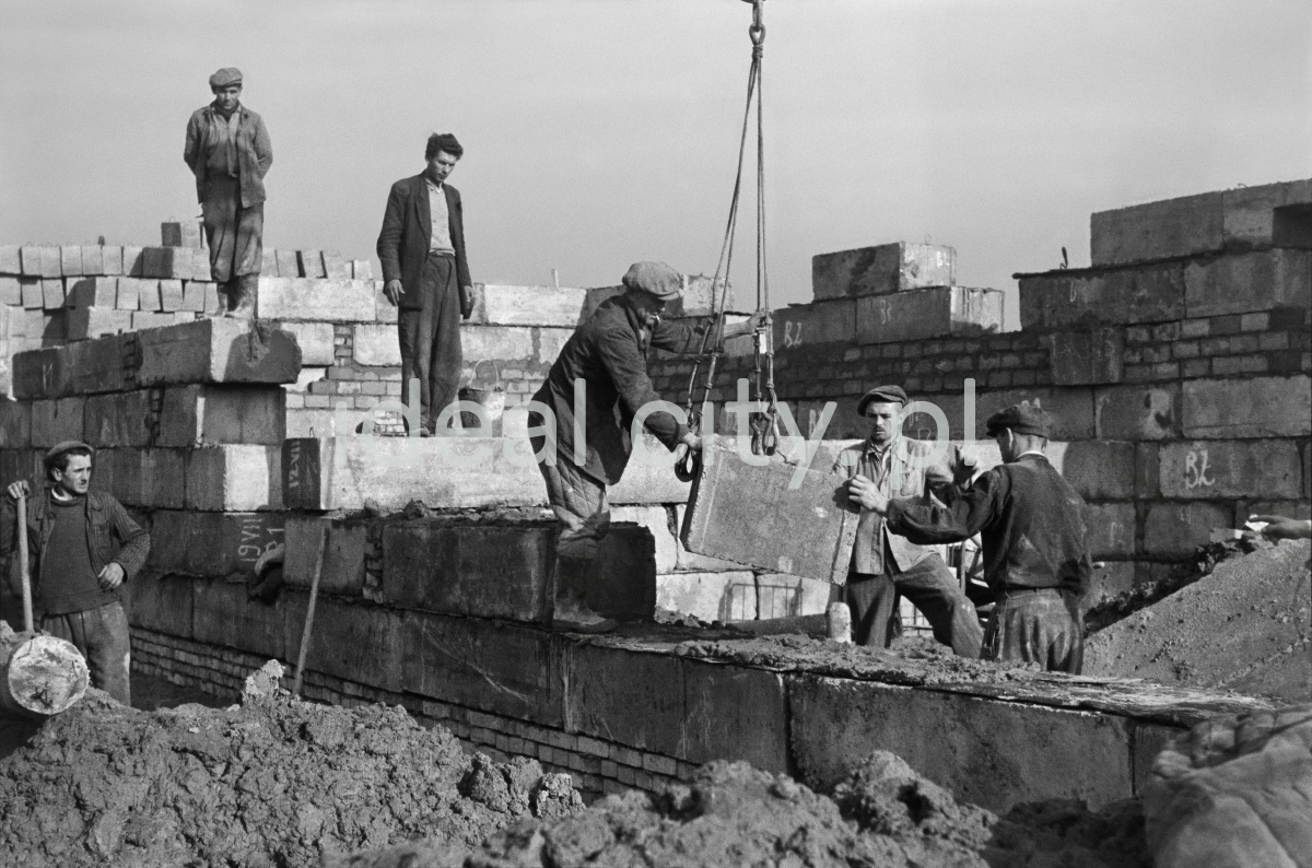 Workers assemble the walls of the building from massive concrete blocks.