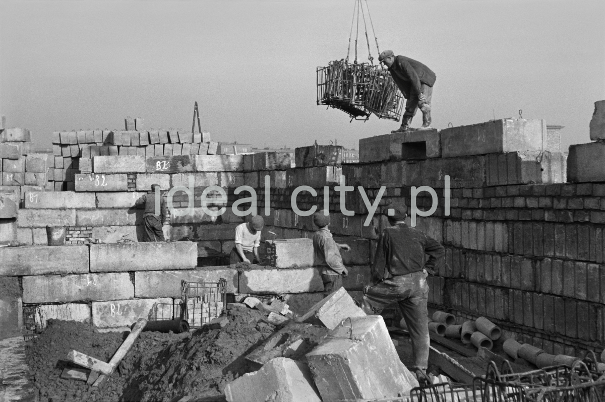 Workers assemble the walls of the building from massive concrete blocks.