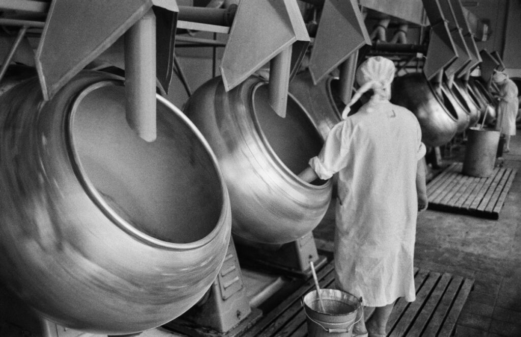 A woman in an apron is mixing with a ladle in rotary boilers.