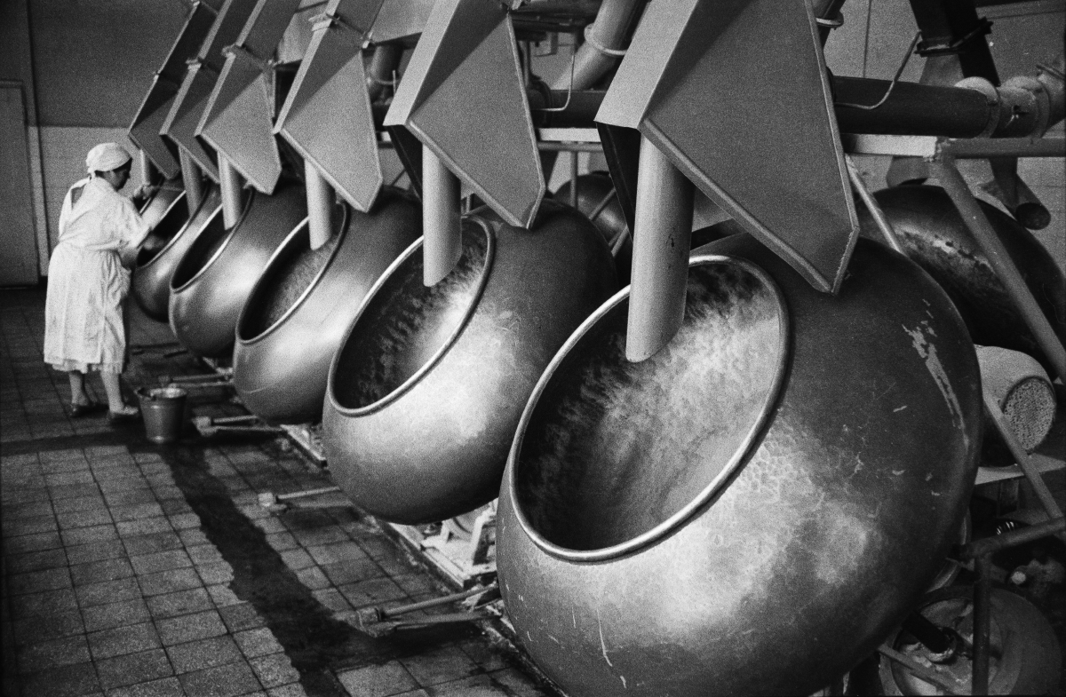 A woman in an apron is mixing with a ladle in rotary boilers.