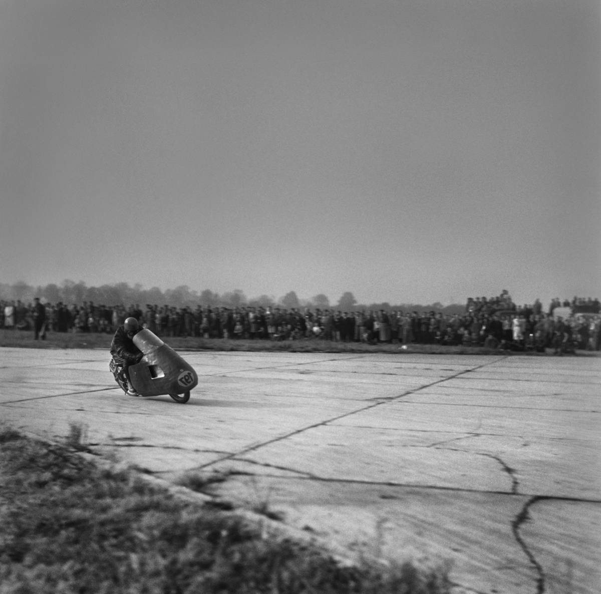 The motorcyclist is driving the bend at high speed, with spectators in the background.