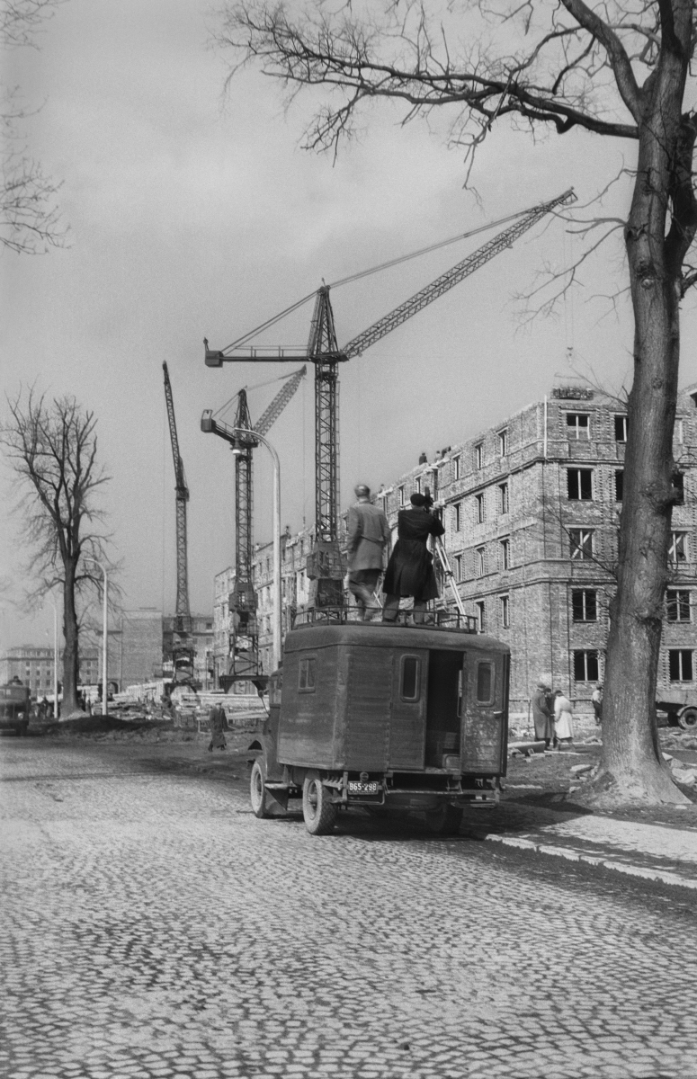 Two men with a tripod and a camera, standing on the roof of a transport car, film residential buildings along the tram line.