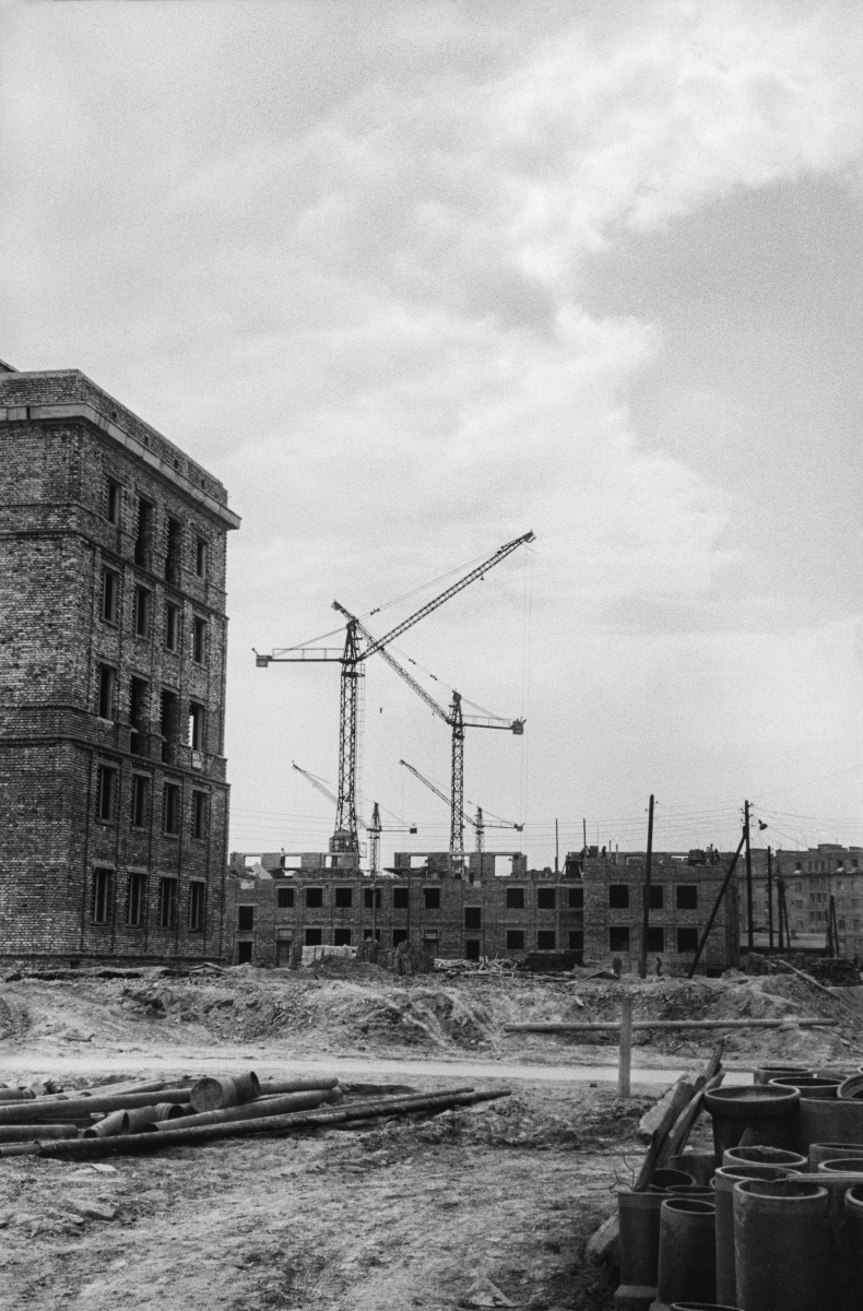 A view of the construction site, on the left, the building is closed, in perspective, the cranes and the construction of the first floors of subsequent blocks.