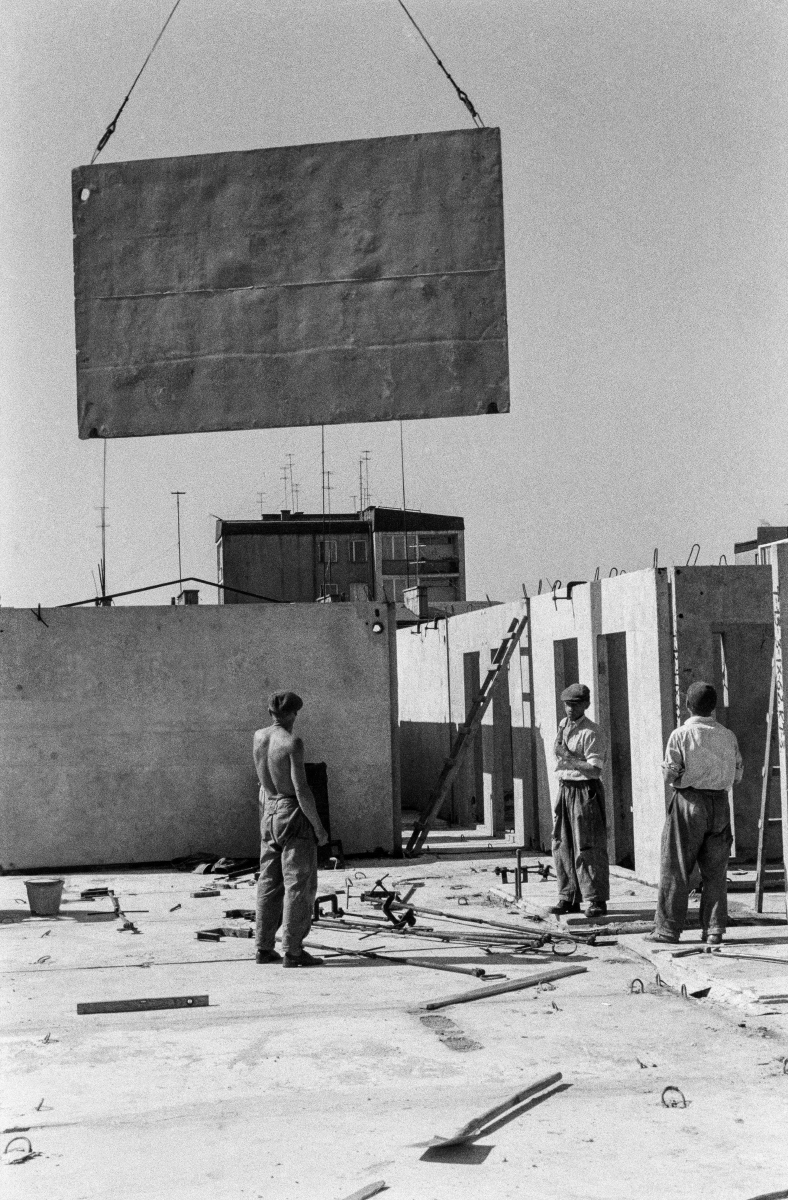 Workers are placing a prefabricated slab on the building's storey, which is fed to them by a crane.