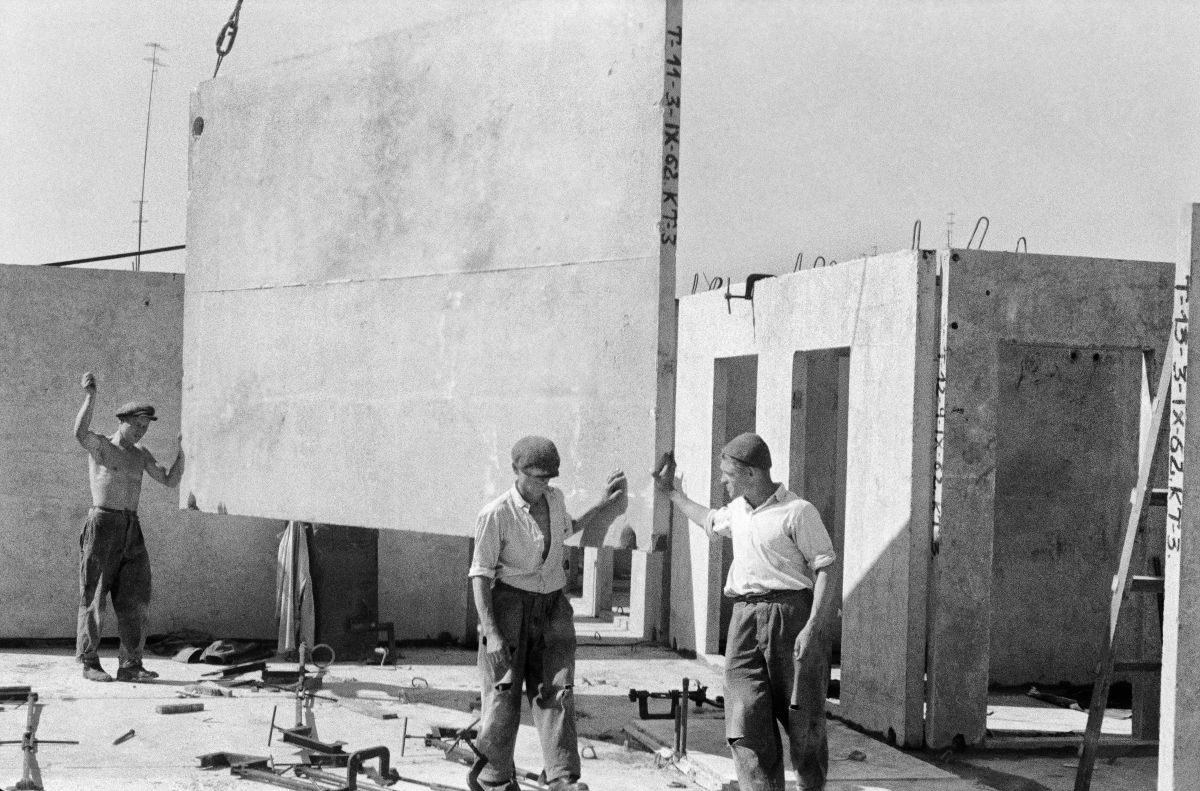 Workers place a prefabricated slab on the building's storey, which is fed to them by a crane.