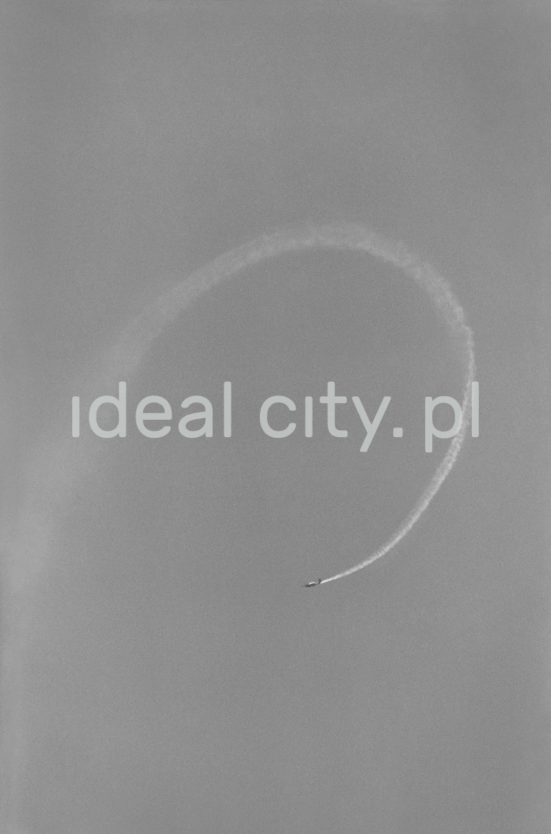 A sports plane performs acrobatics in the sky, leaving a curved trail.