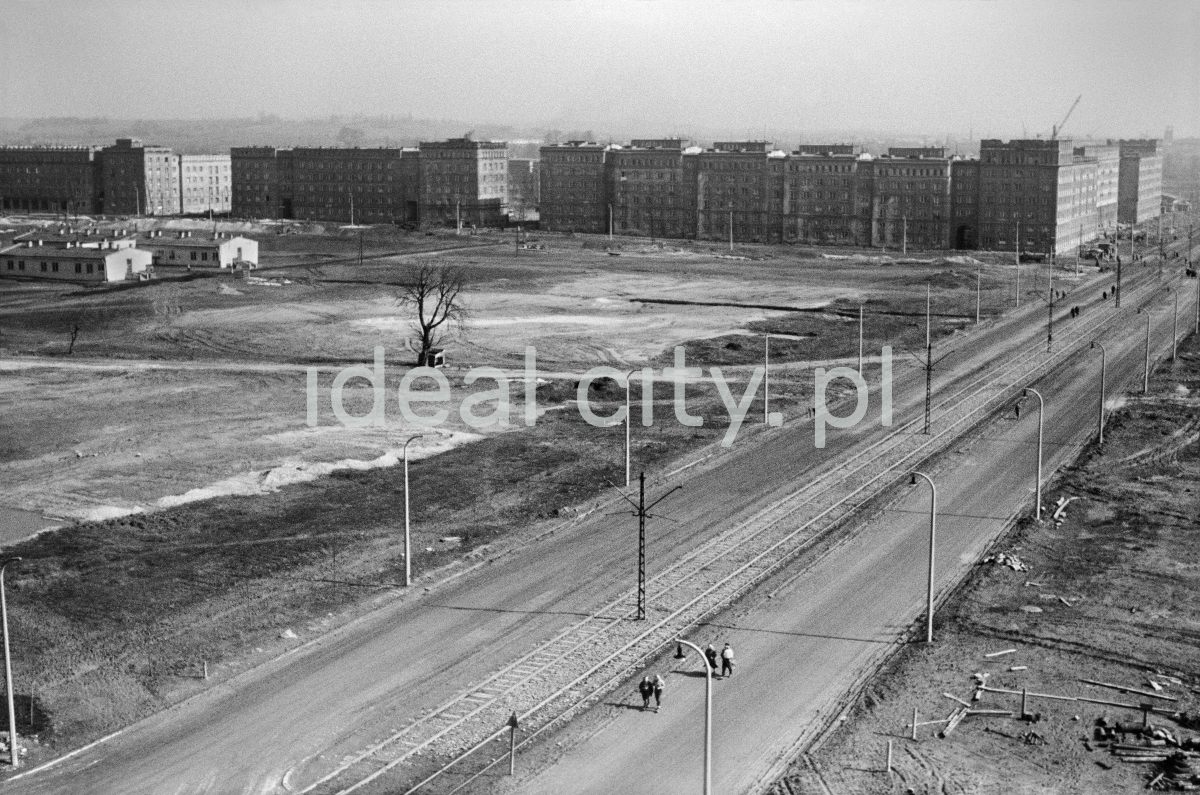 A view from above on the newly created two-lane road with a tramway, on the left an empty, unpaved square, compact buildings in the perspective.