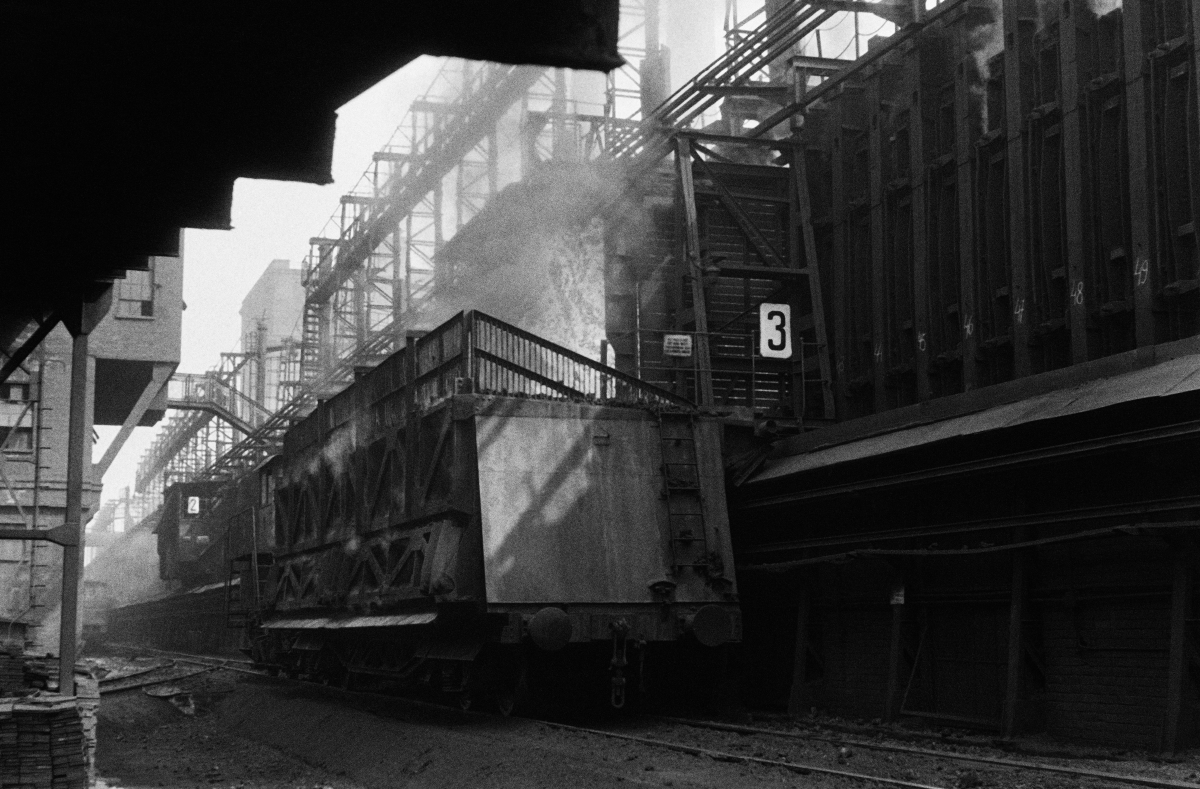 The coke wagon stands on the track next to a massive steel structure.