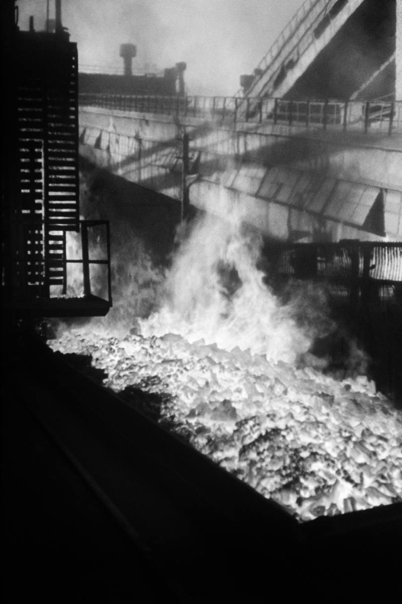 Vertical view of a burning coke heap between the constructions of the plant.