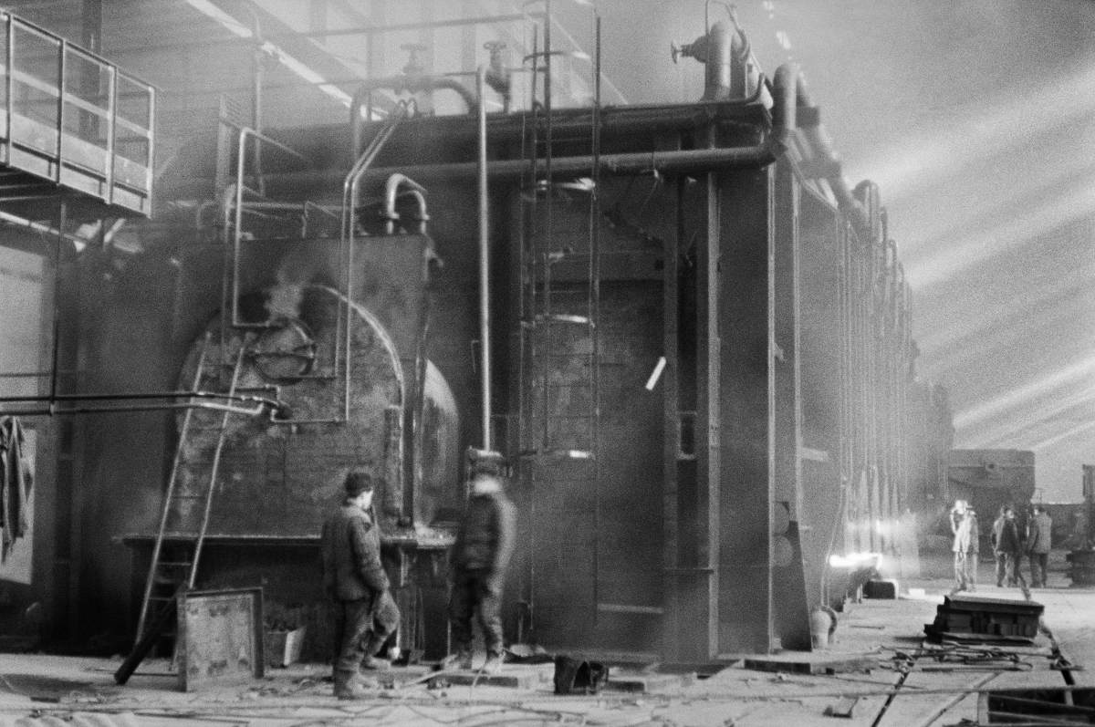 Two men are standing in front of a huge structure in the center of a spacious hall.