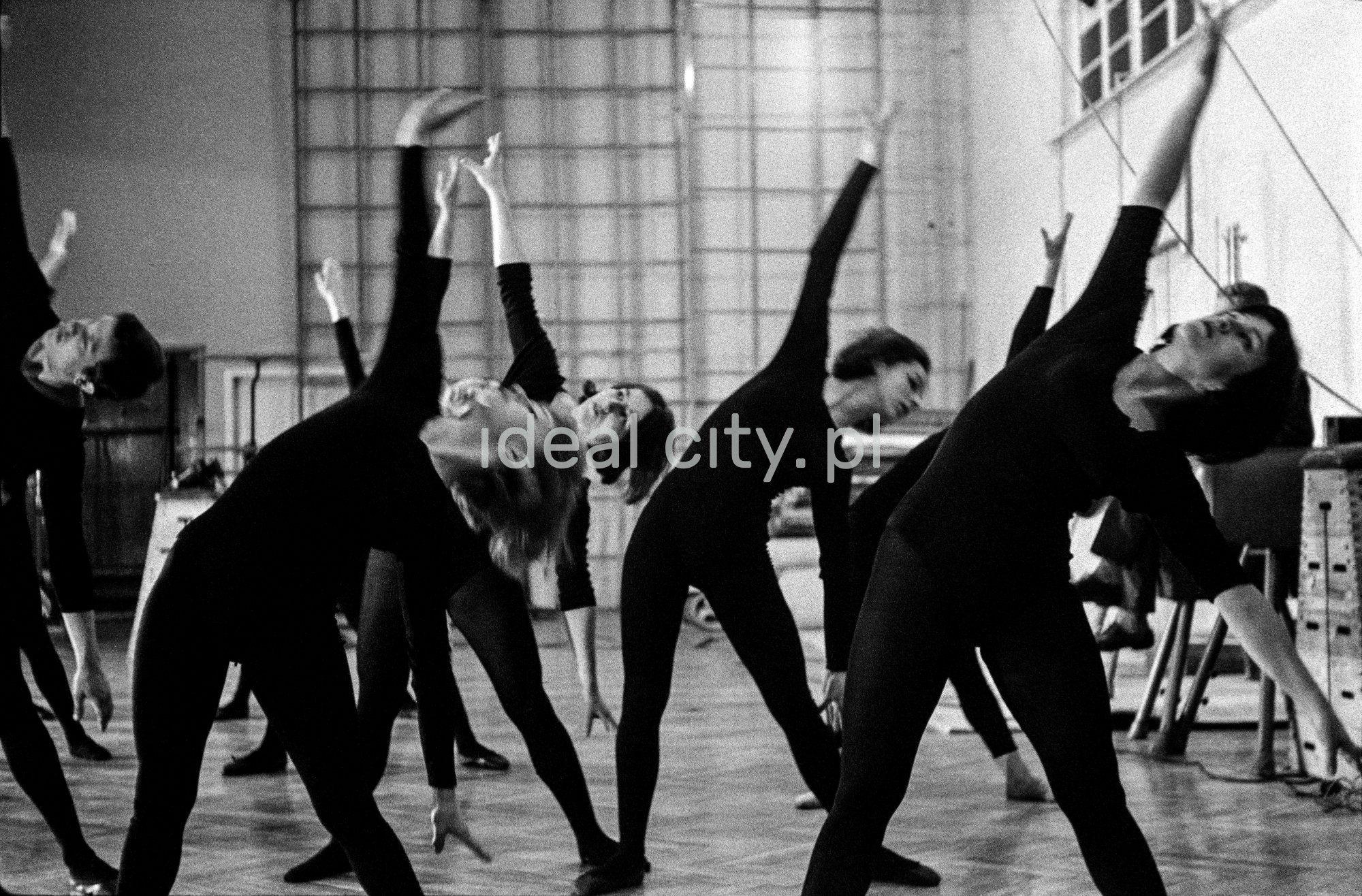 Dancers in black tight costumes lean to the left, lifting their right arms up.