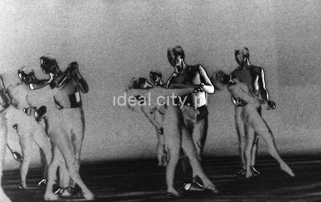 A group of dancers in tight-fitting costumes perform a collective figure on stage with a black background. The negative was solarized.