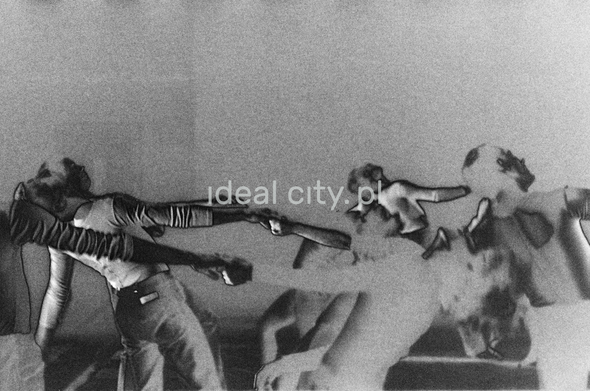 A group of dancers in tight-fitting costumes perform a collective figure on stage with a black background. The negative was solarized.