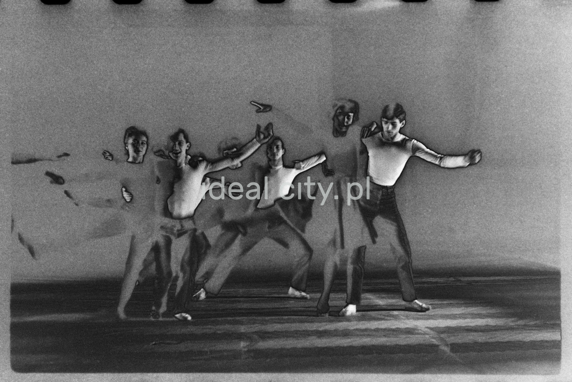 A group of dancers in tight-fitting costumes perform a collective figure on stage with a black background. The negative was solarized.