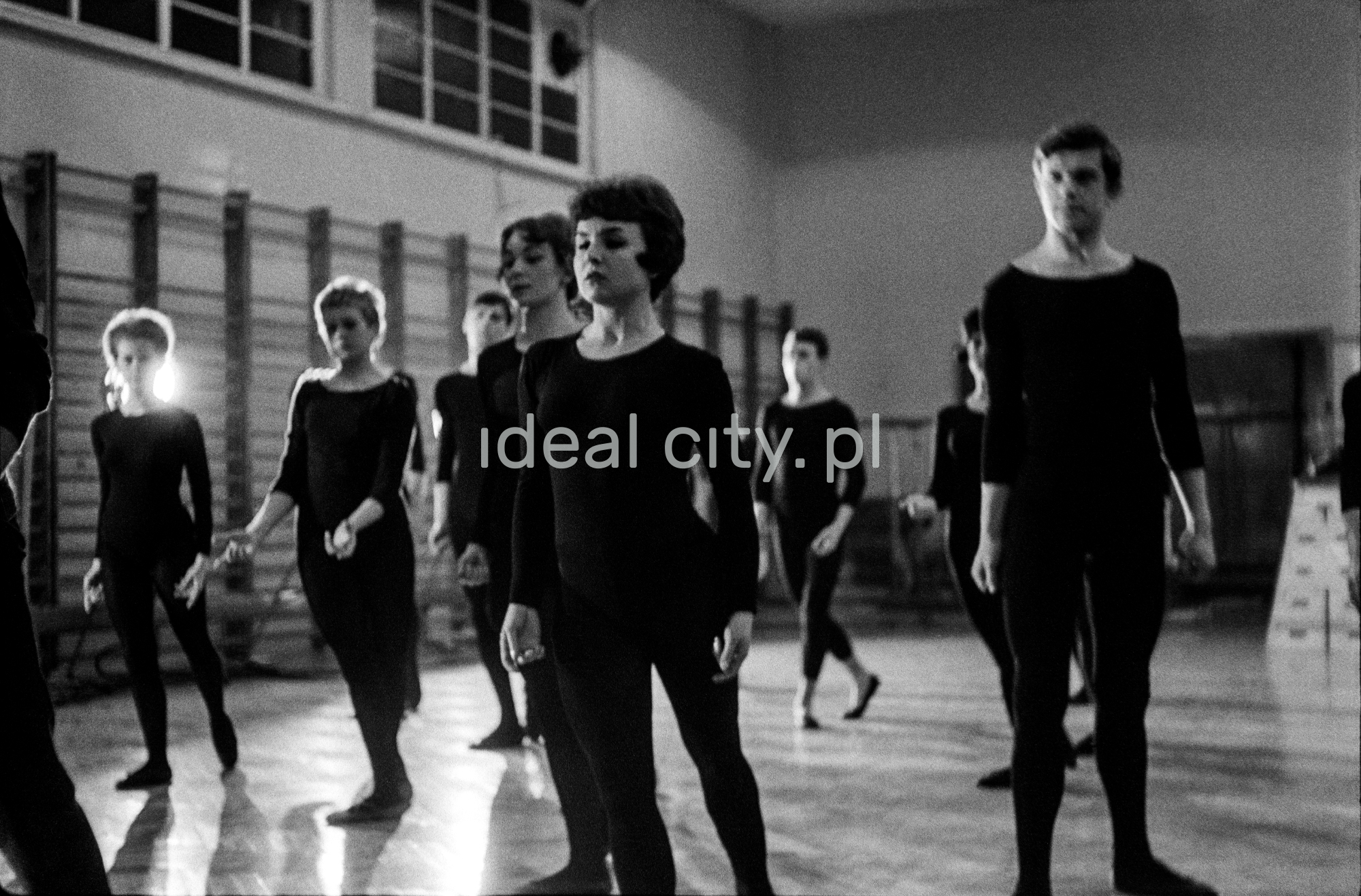 Dancers in black tight fitting clothes look straight ahead.