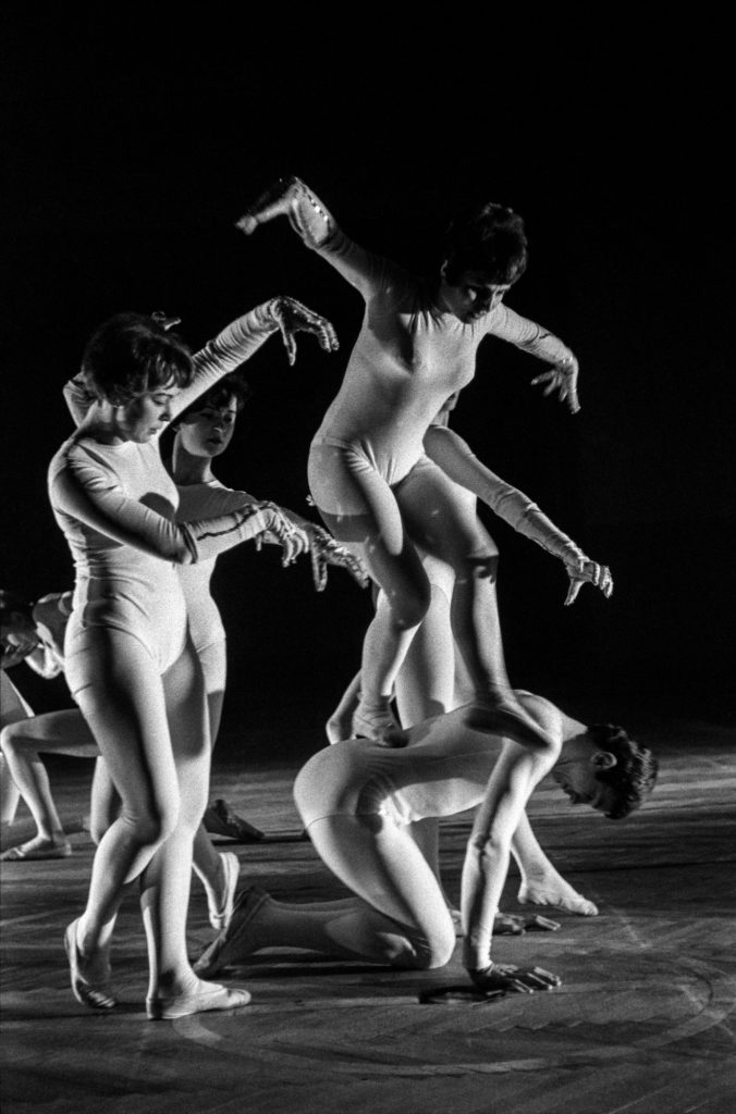 Tancerze w białych, obisłych strojach wykonują zbiorowe figury taneczne