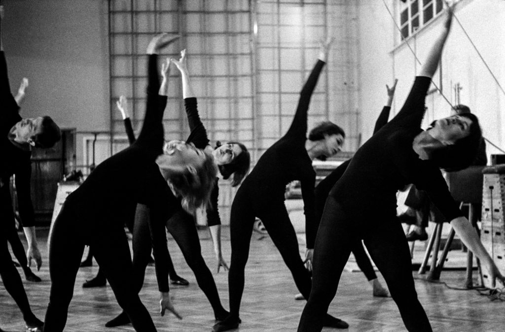 Tancerze w czarnych, obisłych strojach wykonują zbiorowe figury taneczne