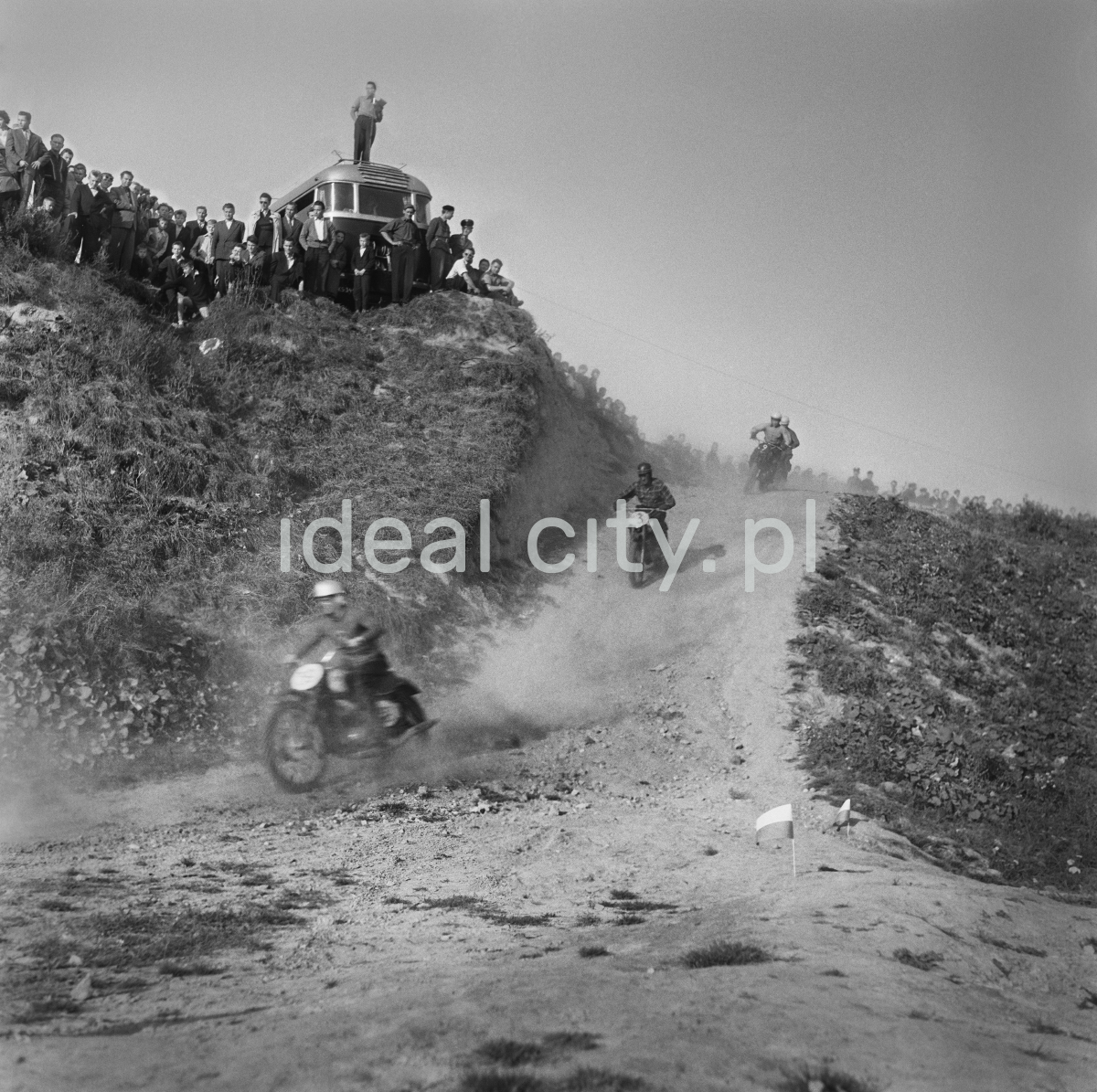 Motorcyclists descend from the hill and the onlookers are watching.