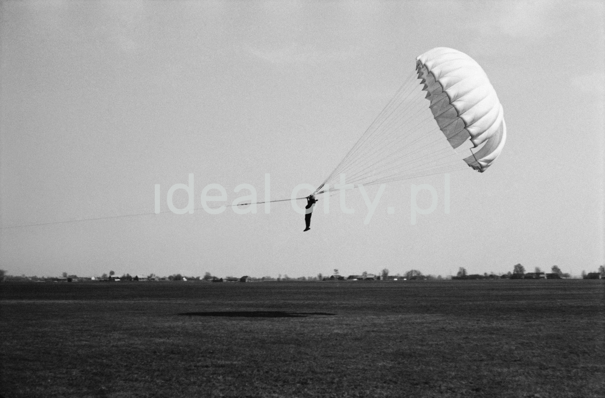 The paratrooper with the taut parachute rises at an angle, tethered just above the ground.