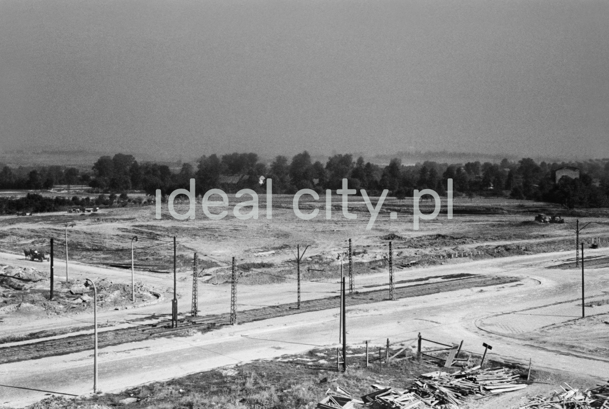 A view from above on an empty square crossed by a tram line, in the background a line of trees.