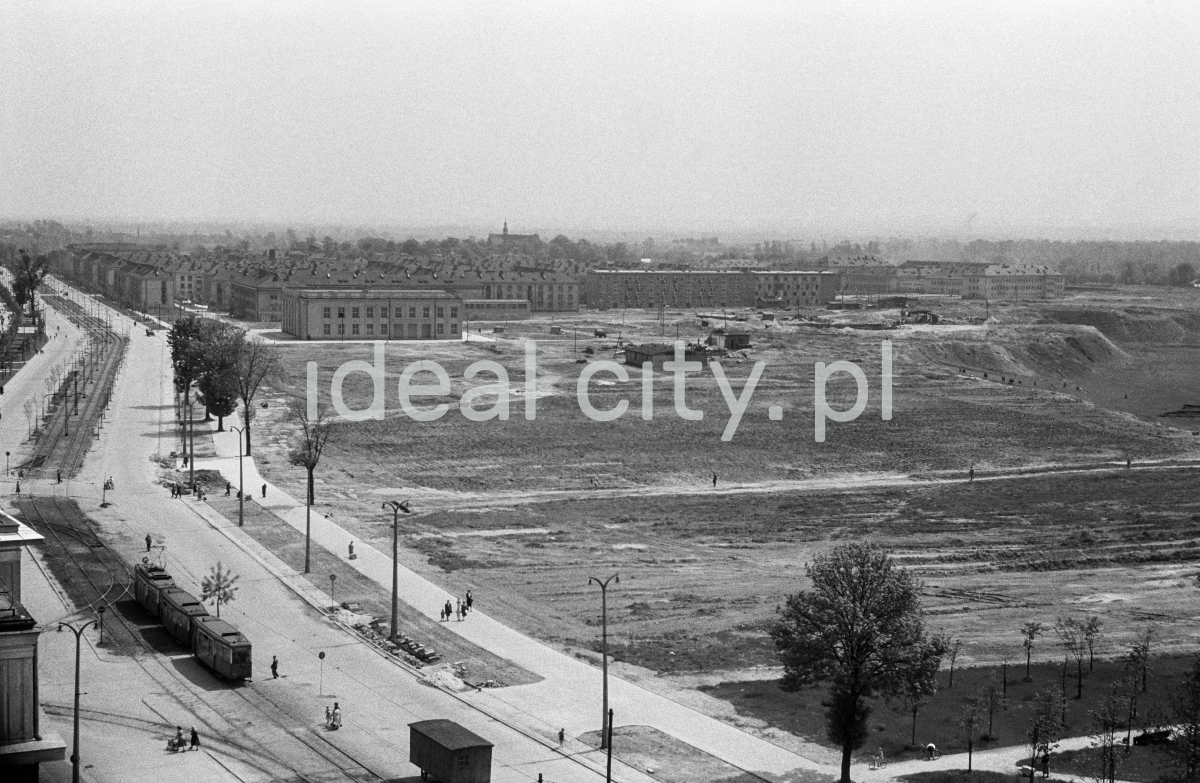 A view from above on a wide avenue with tram traffic, on the right meadow areas, housing development in perspective.