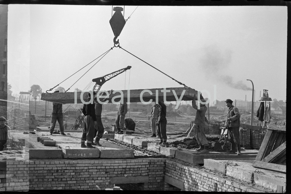 Workers pick up a prefabricated concrete slab fed to them by a crane.