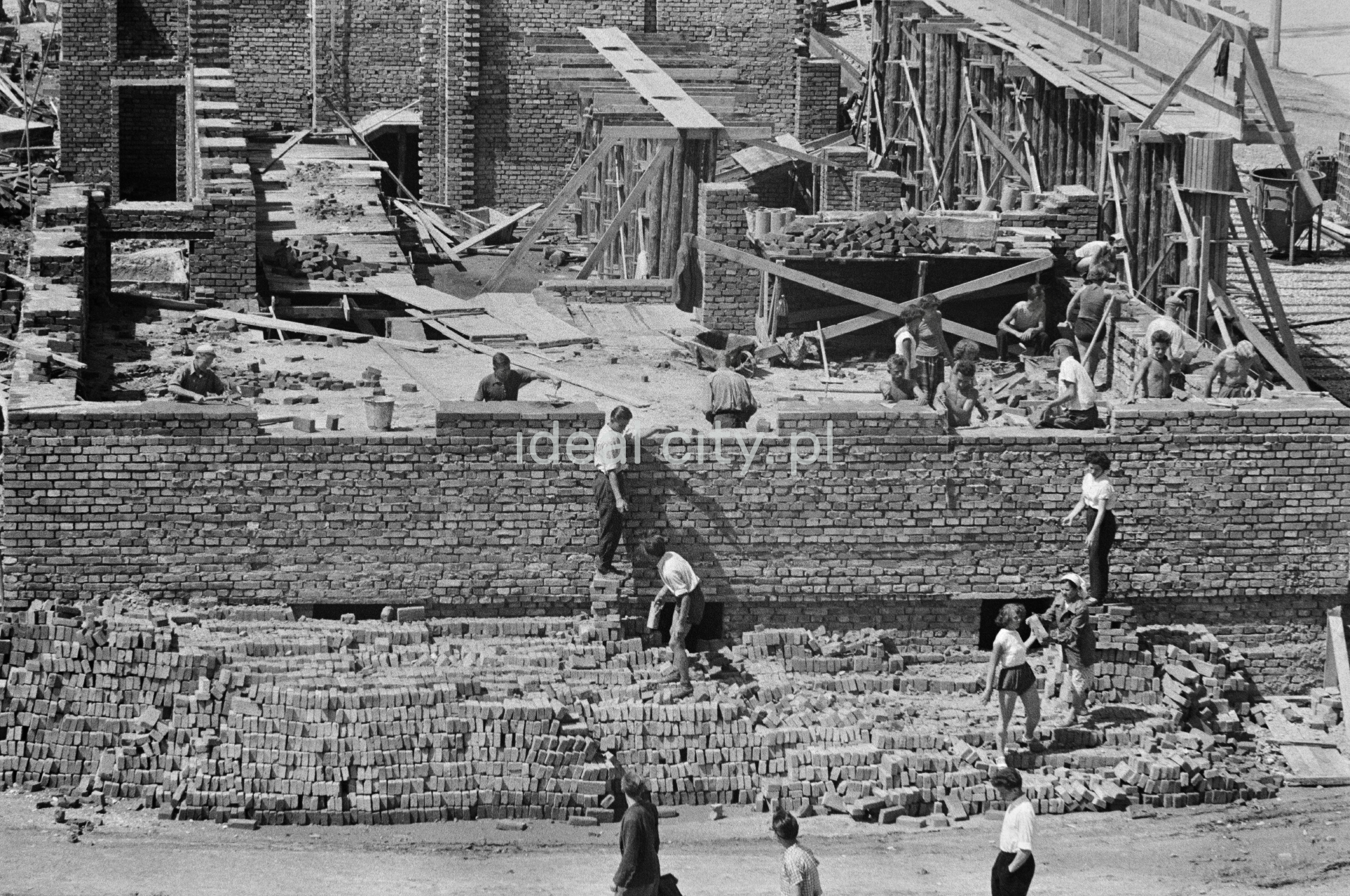 People in everyday clothes are passing bricks along the brick wall of the building.