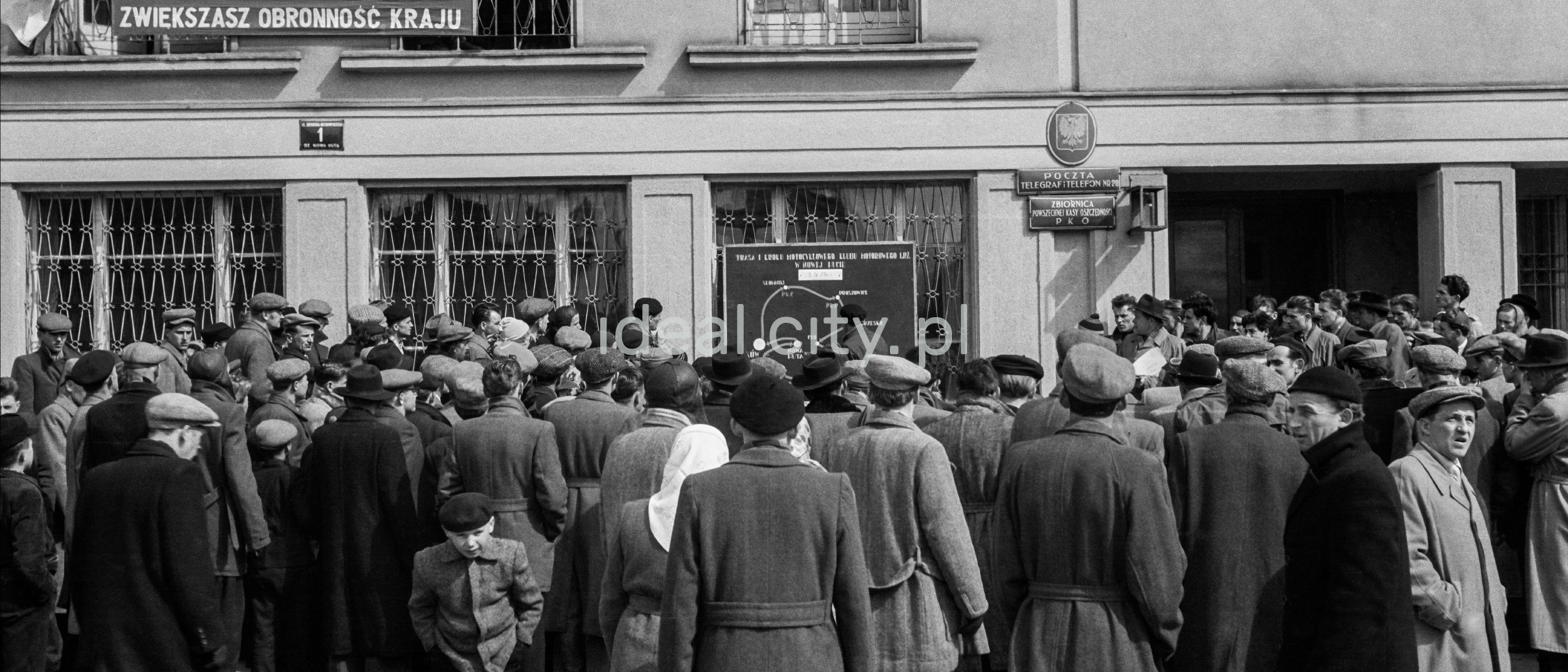 A crowd of men in coats and caps gathered in front of the office building.
