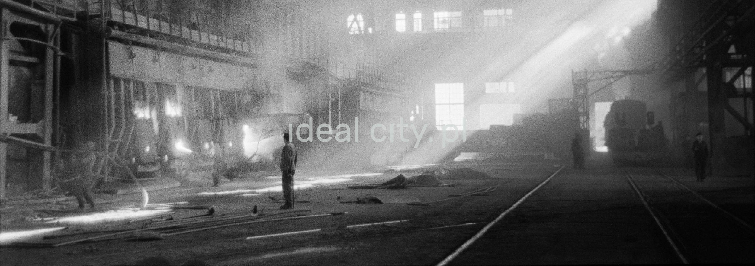 A man in the middle of a factory hall where the sun shines through fireflies.