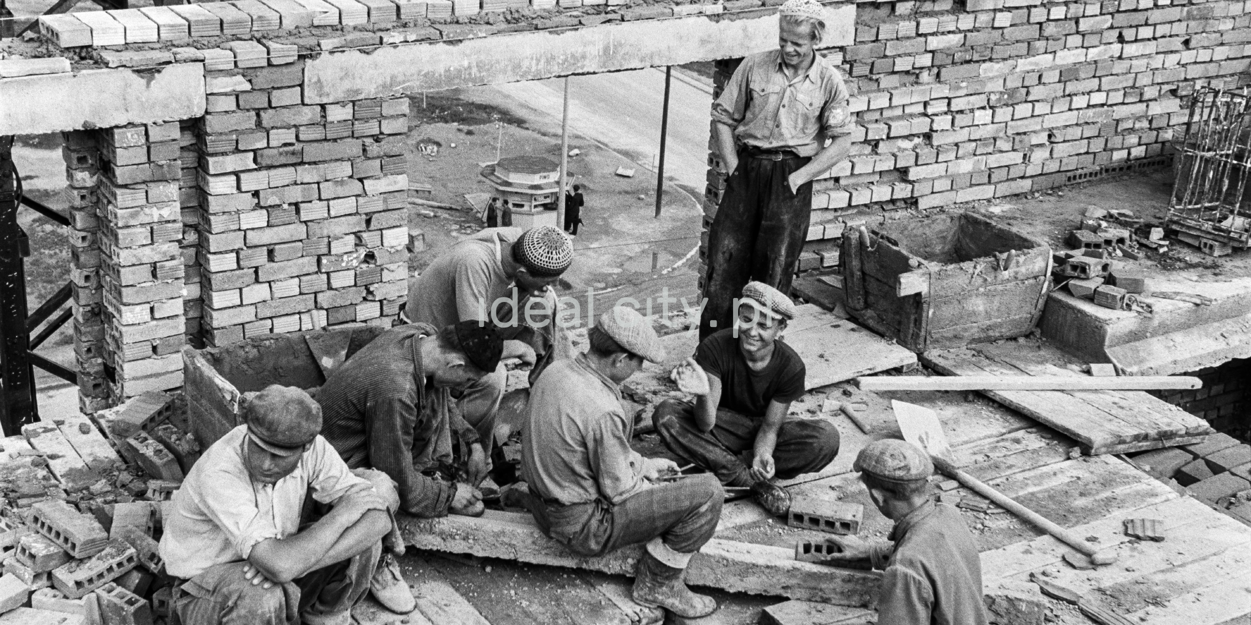 The bricklayers rest during construction on the first floor of the building. Between them, at the level of the pavement, a beer booth is visible.