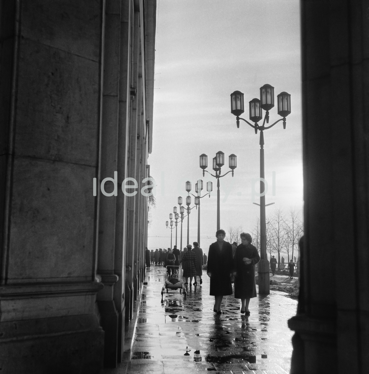 Pedestrian traffic on the promenade of the central square, next to the monumental arcades. Shot after the rain, against the sun.