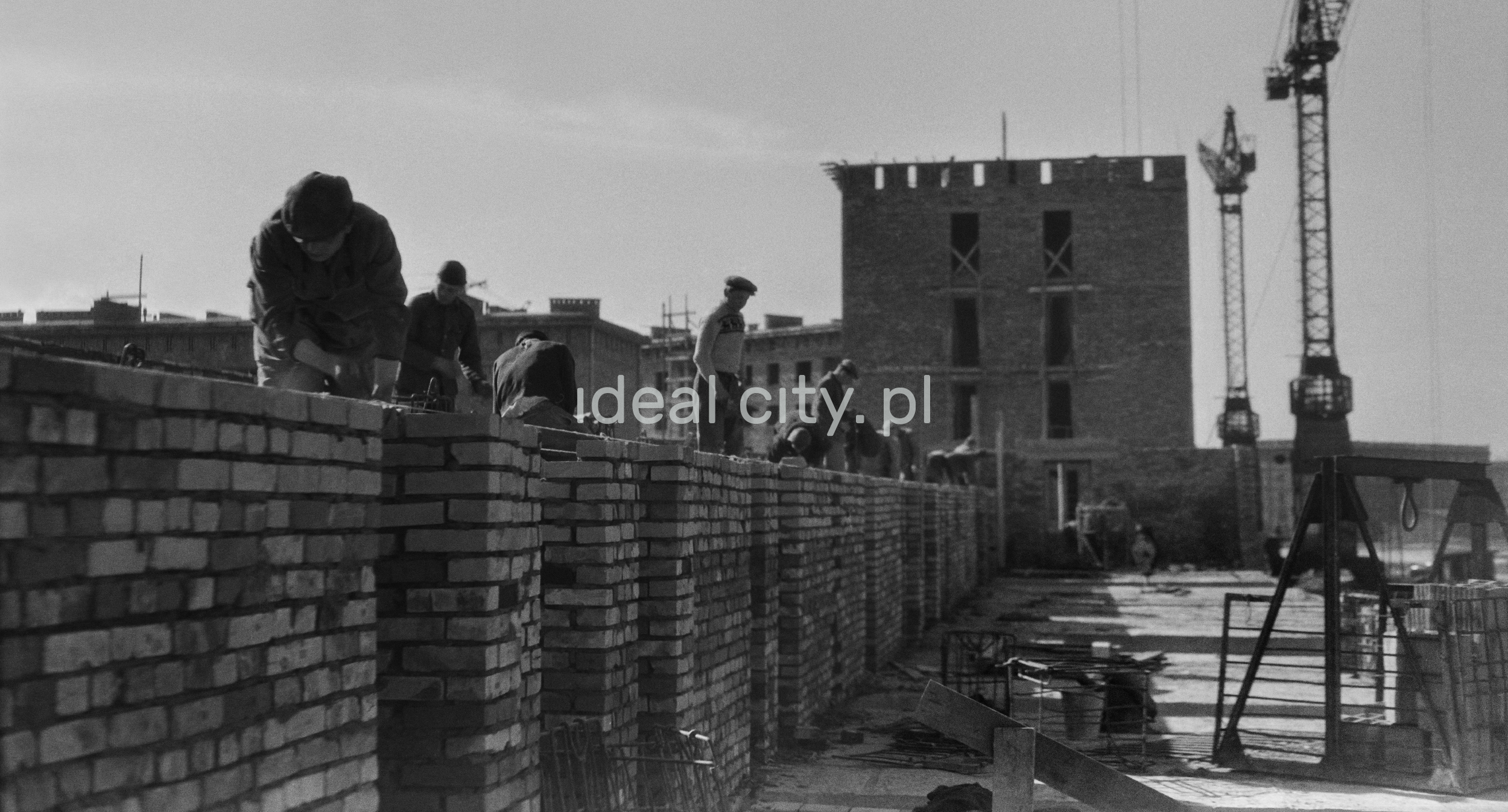 A shot against the light shows bricklayers putting up a building wall.