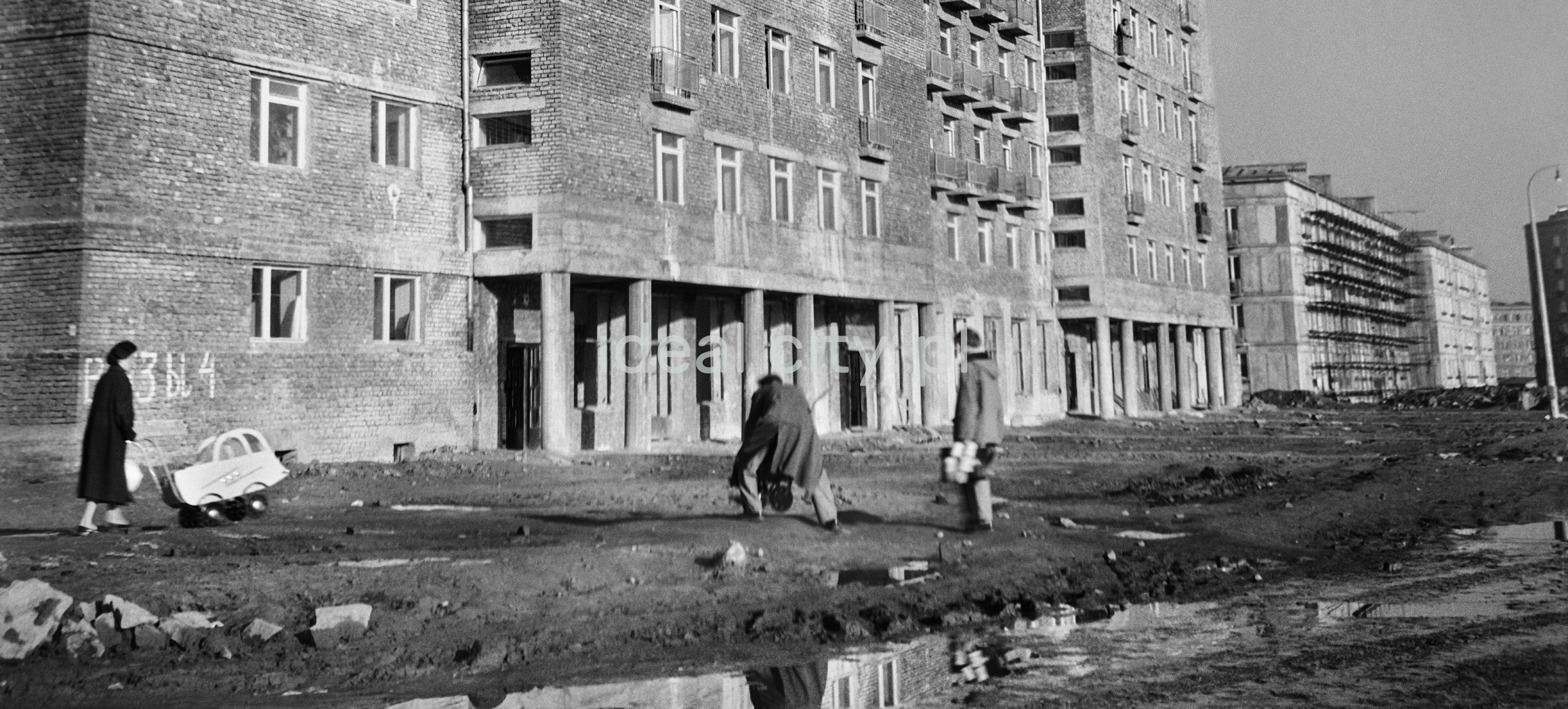 Parents with children in front of an unplastered apartment block.