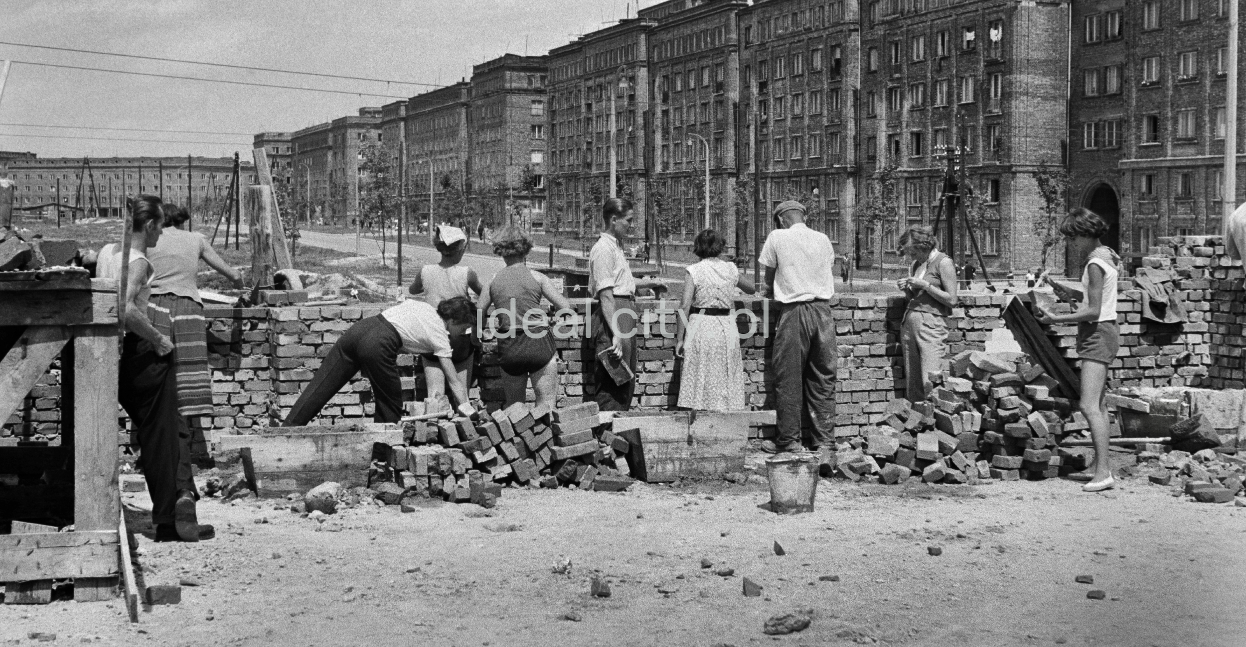 A group of people in everyday clothes is building a brick wall on the ground floor level.