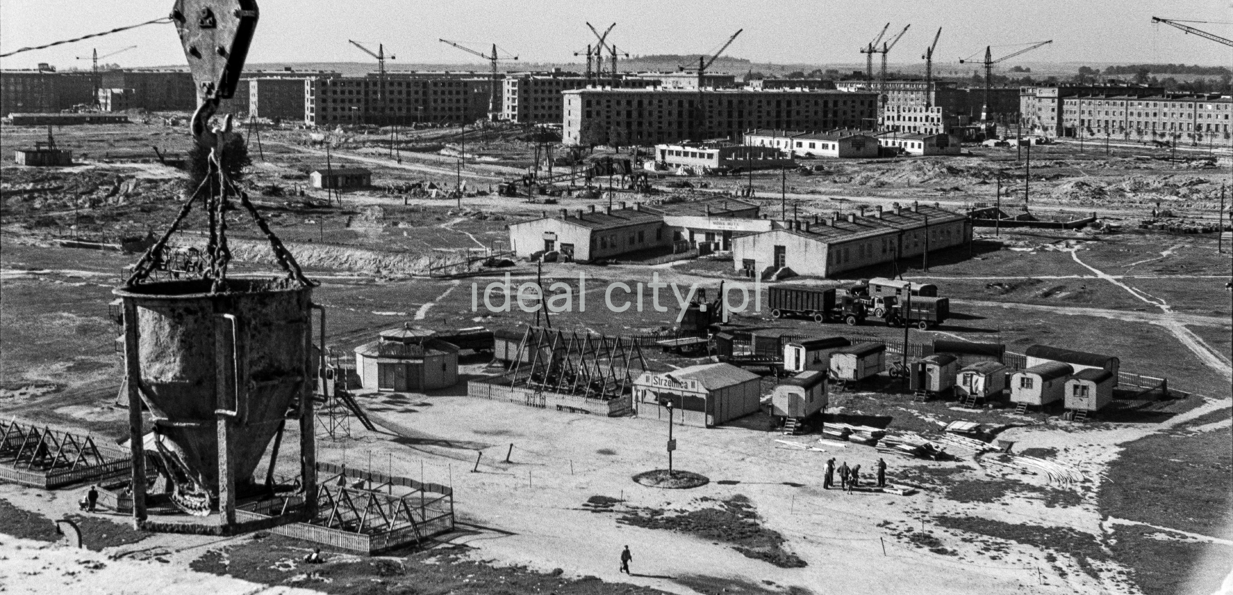 A view of the building barracks from above, in the foreground a pear with concrete hanging from a crane.