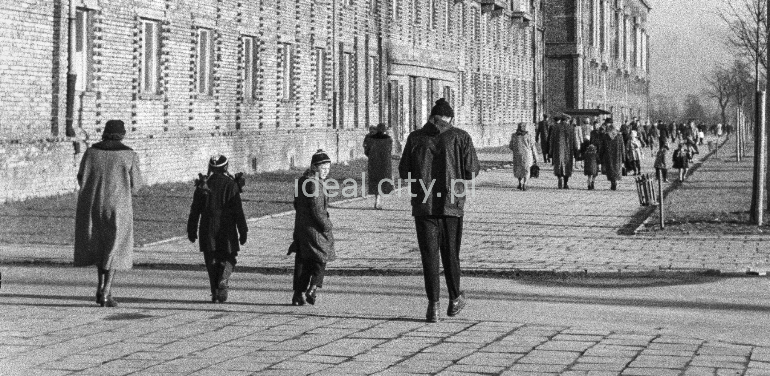 Rear shot of pedestrians walking along a wide sidewalk.