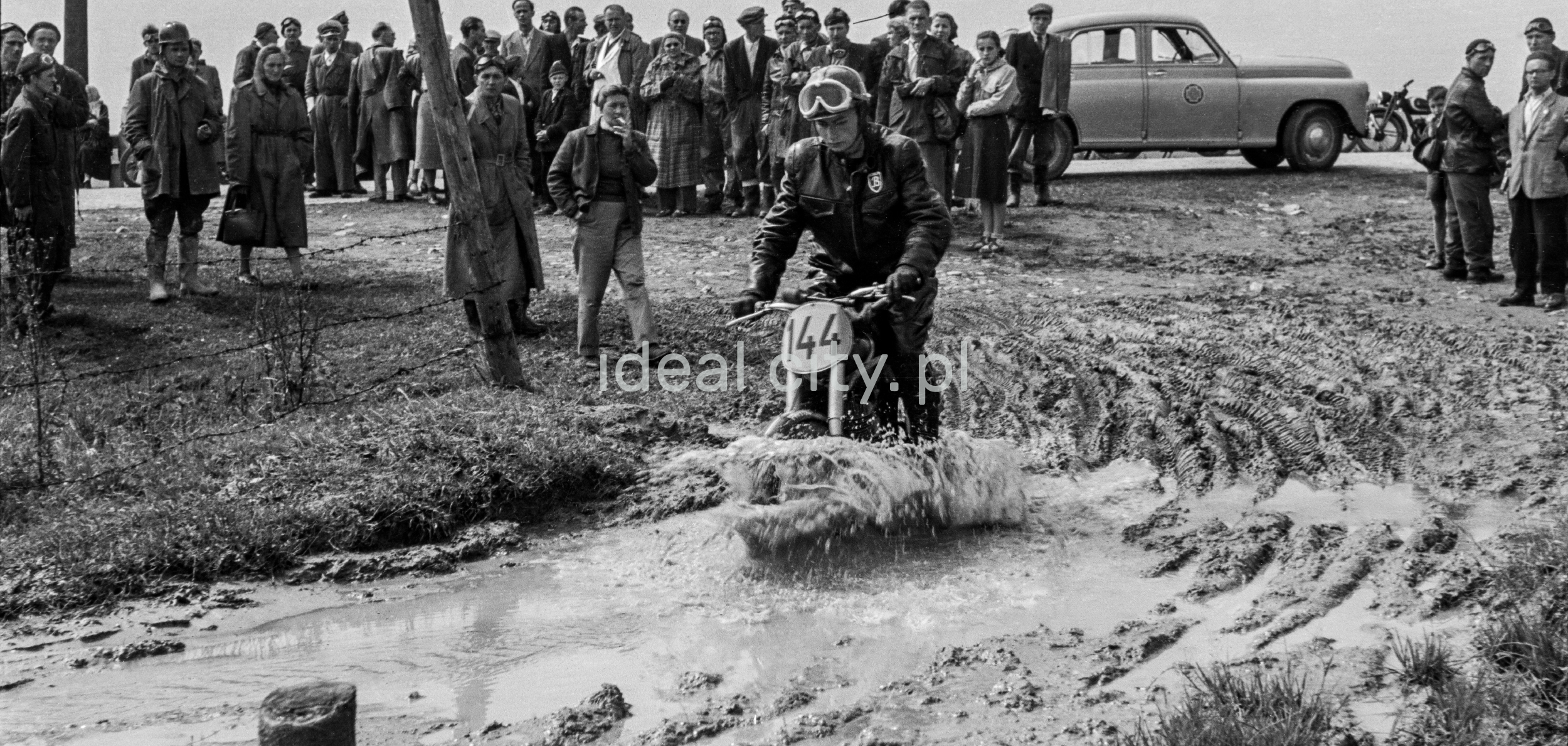48/5000 The motorcyclist drives into a mud ditch with onlookers in the background.
