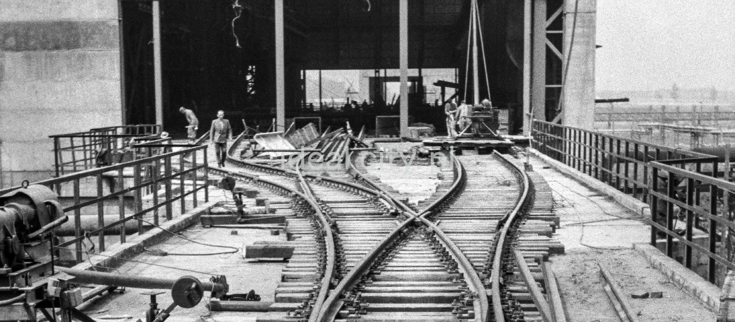 Perspektywa plątaniny torów kolejowych prowadzących do hali fabrycznej.