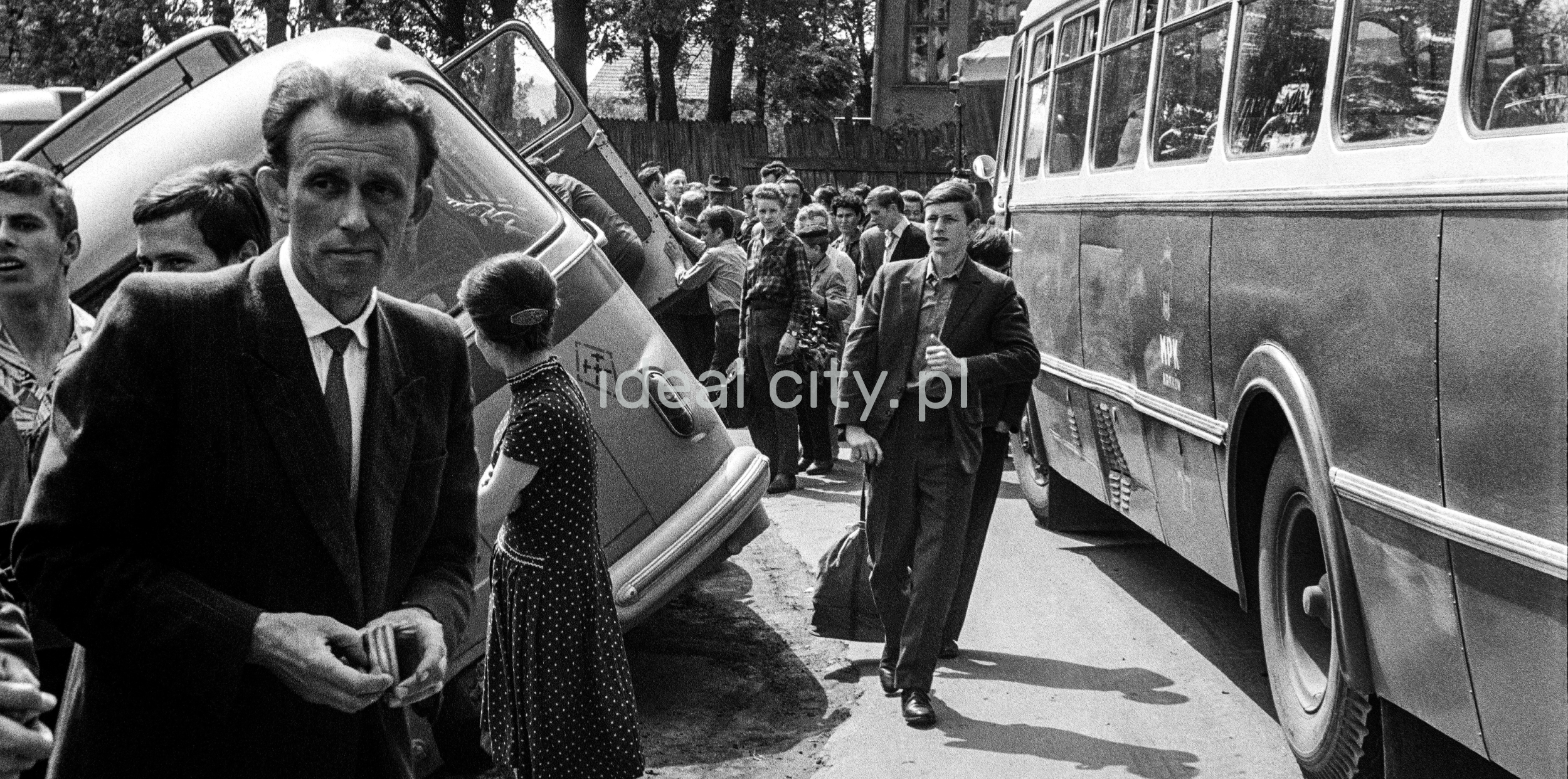 Passengers in suits walk between the bus that is overturned on its side and another stopped on the road.