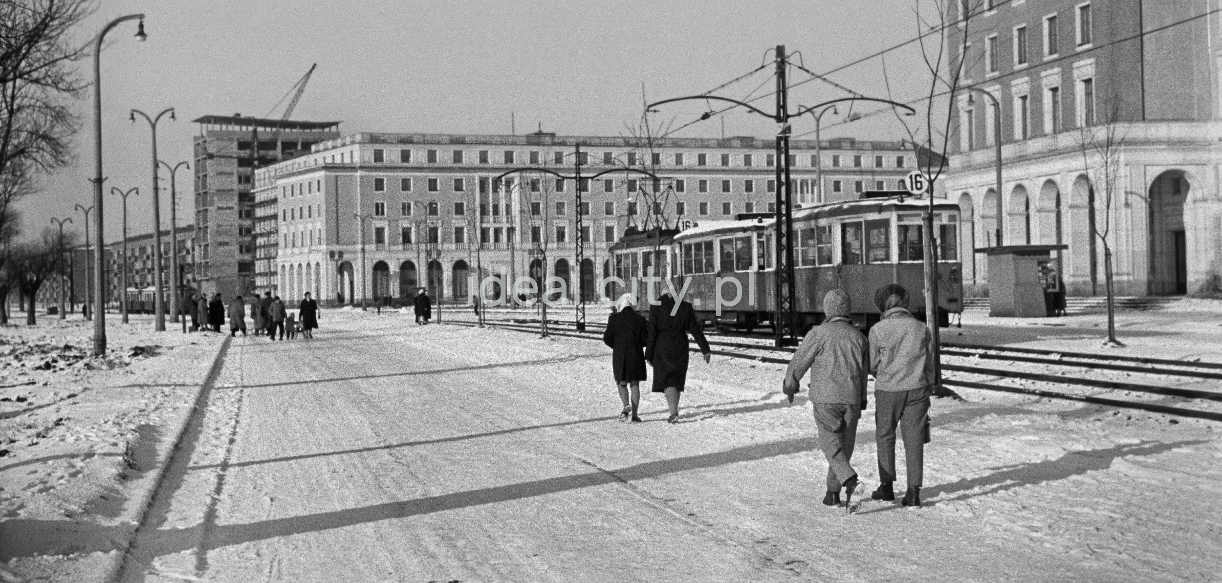 Pedestrian traffic on a snowy street, monumental apartment blocks in the background.