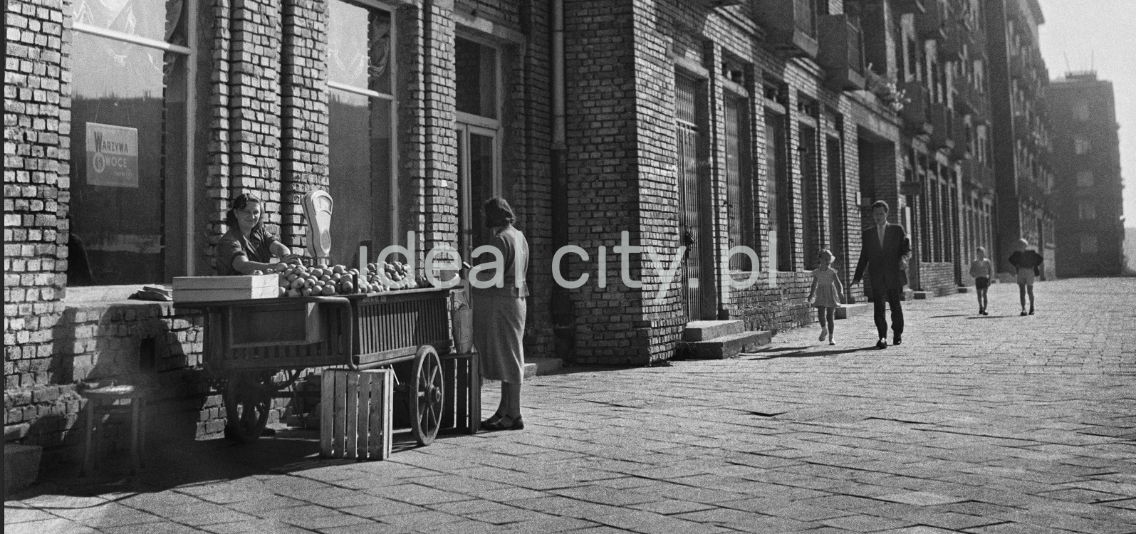 Fruit stand on the wide sidewalk in front of the vegetable store.