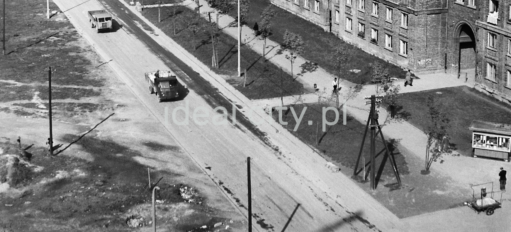 Top view of the road where two cars are driving, a pavement on the right, a kiosk booth and pedestrians.
