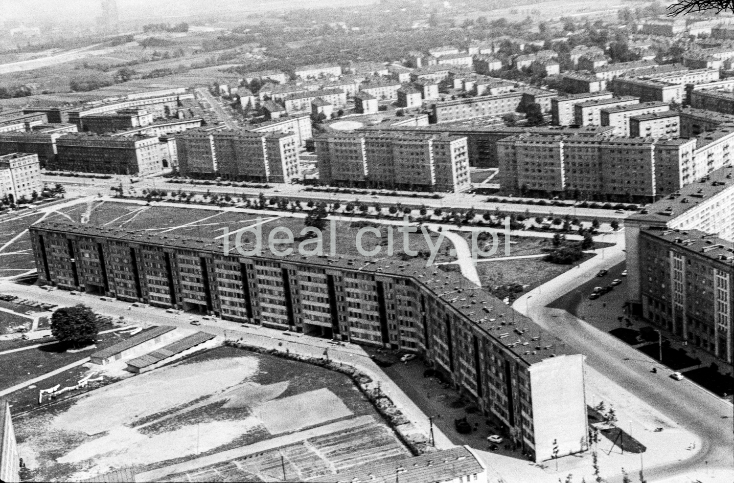 A bird's-eye view of a wide, low apartment block, the perspective of successive blocks in the background, and the spaces and paths trampled by the inhabitants.