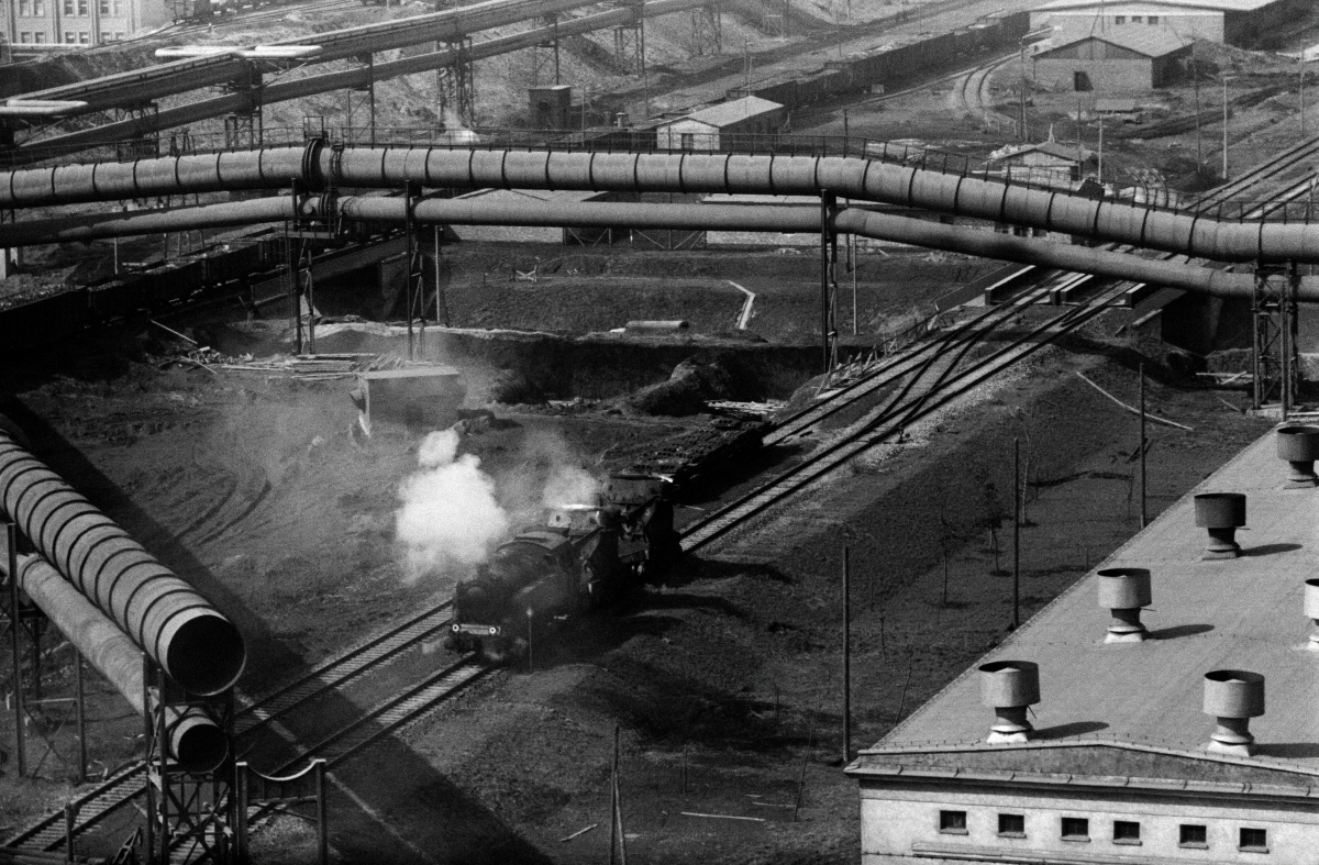 A top view of the tangle of pipelines, with a diesel locomotive passing between them.