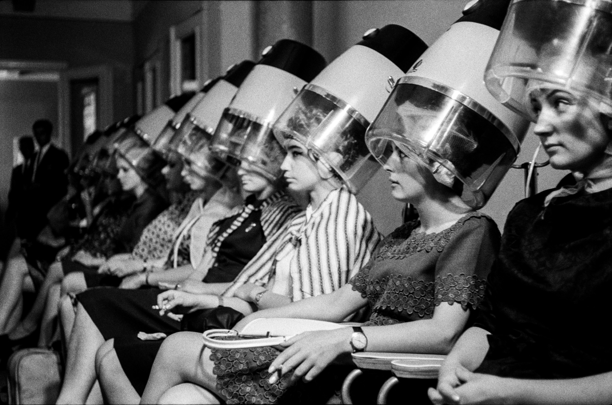 The women sit in a row under the hair dryers.
