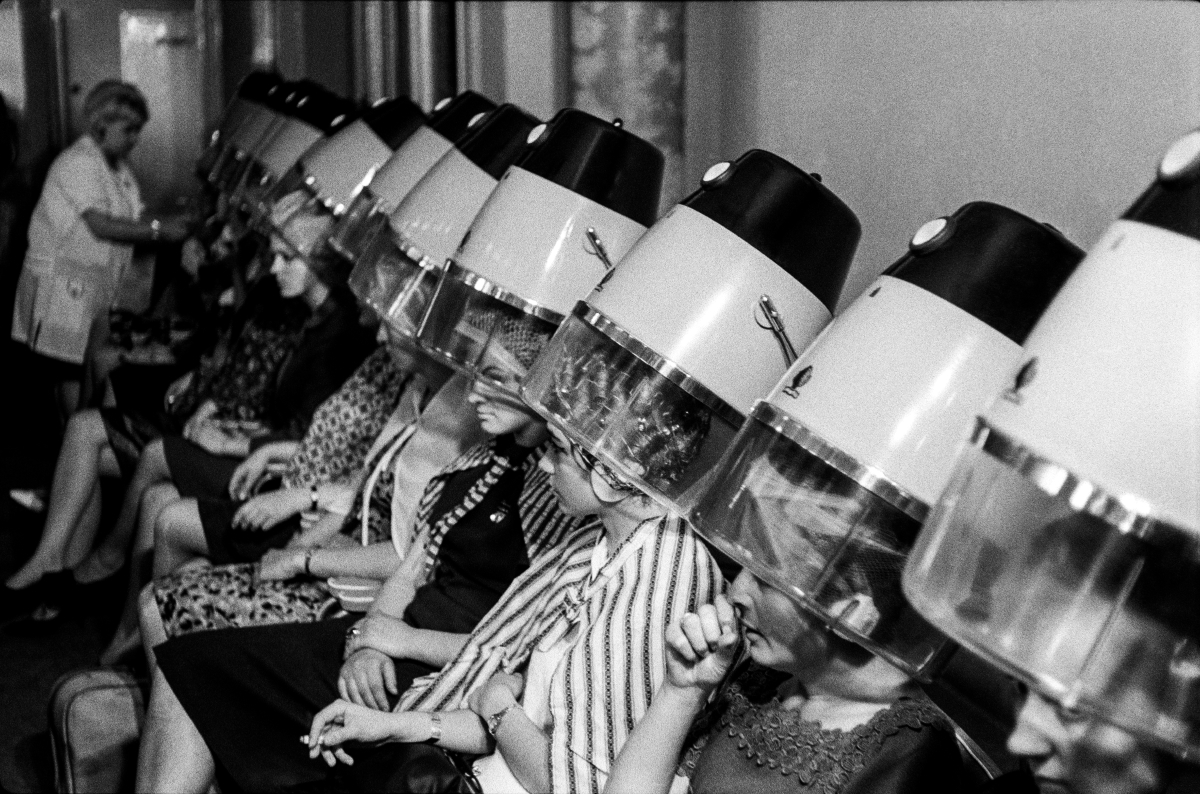 The women sit in a row under the hair dryers.