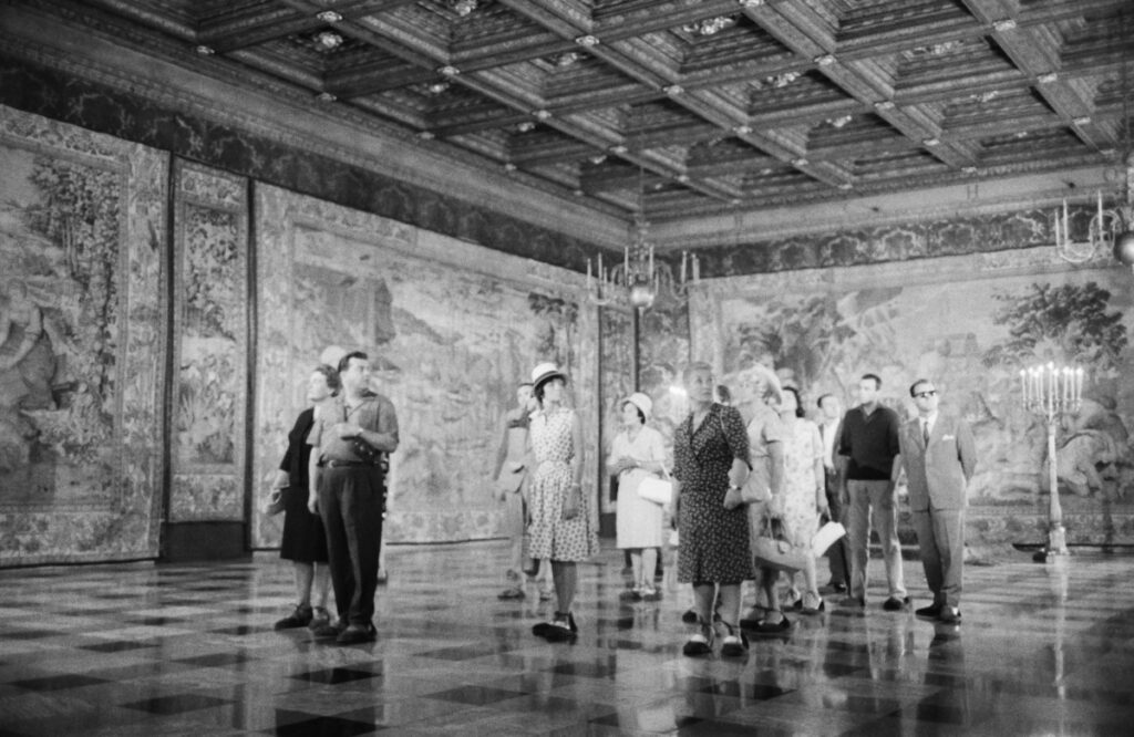 A group of tourists is examining the tapestries on the walls of a spacious room.