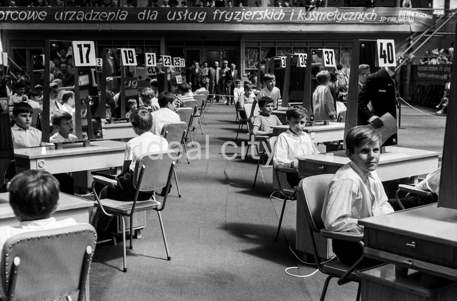 Boys in white shirts are sitting at two rows of tables with numbers.